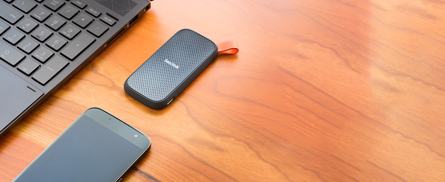 SanDisk Portable SSD on a desk next to a laptop keyboard and smartphone